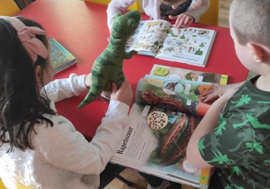 Dzieci oglądają zdjęcia i czytają ciekawostki o dinozaurach.